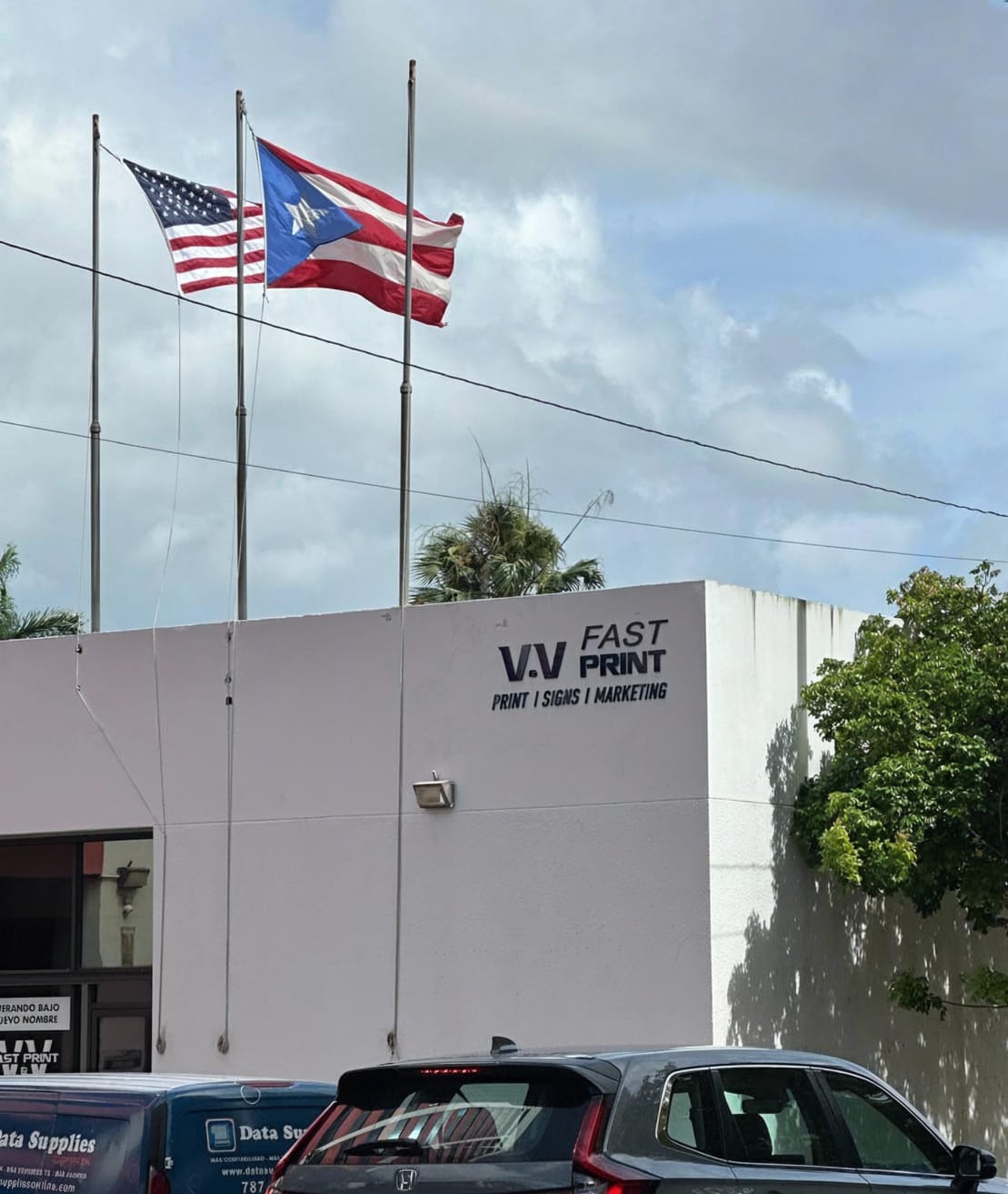 Fachada de V&V Fast Print con las banderas de EE.UU. y Puerto Rico
